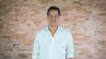 Daniel Nathrath, CEO von Ada Health, steht lächelnd in einem weissem Hemd vor einer Backsteinmauer.