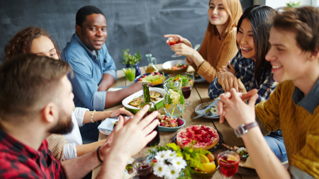Eine Gruppe von sechs Personen sitzt um einen Tisch und geniesst gemeinsam Essen und Getränke.