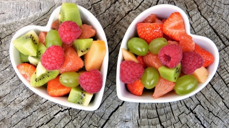 Two heart-shaped bowls filled with colourful fresh fruit.