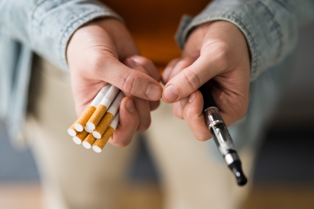 Eine Person mit mehreren Zigaretten in der einen und einem Vape Pen in der anderen Hand, die die Wahl zwischen traditionellem Rauchen und Vaping nahelegt.