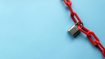 Un cadenas argenté retient une chaîne en plastique rouge vif qui s'étend en diagonale sur un fond bleu clair. Le cadenas est suspendu près du coin supérieur droit, tandis que le côté gauche de l'image est vide.